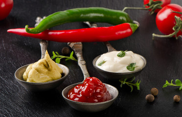 Mustard, ketchup and mayonnaise on black table.