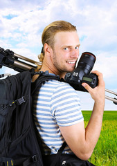 Young photographer with camera and tripod on nature background