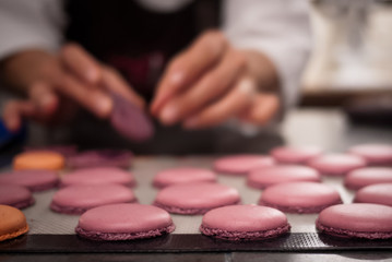 Baker placing macaron cookies on sheet for baking, with baker bl