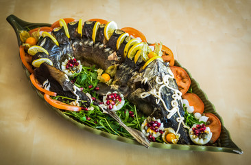 Sturgeon decorated with lemon and tomatoes on a green plate