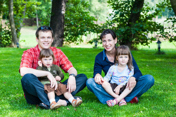 Happy family of four sitting on grass