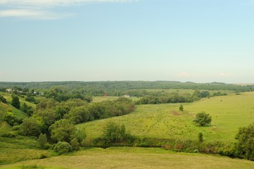 Green meadows near small river with blue sky and forest