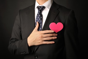 ピンクのハートを持っている黒いスーツの男性の上半身