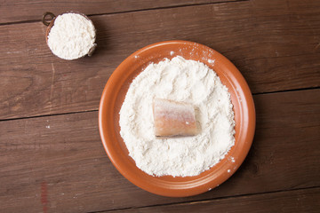 One piece of fresh fish with flour on a plate on a wooden backgr