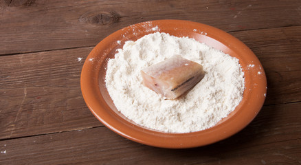 One piece of fresh fish with flour on a plate on a wooden backgr