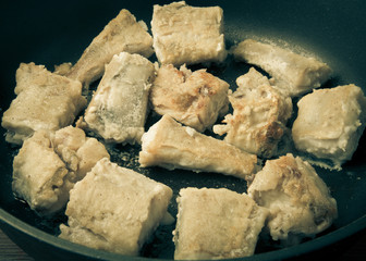 Some pieces of fried fish filet in a frying pan. Toned