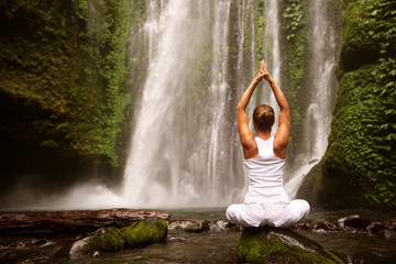 young woman doing yoga in a forest near waterfall