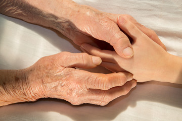 hands of grandmother and grandchild in the bed