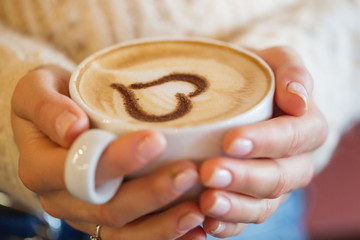 woman holding hot cup of coffee, with heart shape