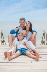 Fototapeta premium happy family sitting on a wooden pontoon in front of the sea