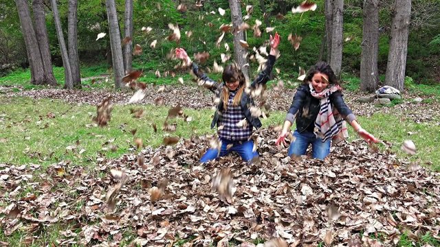 two teens  throw autumn leaves