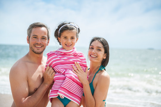 A couple at the beach posing in swimsuits with their daughter 