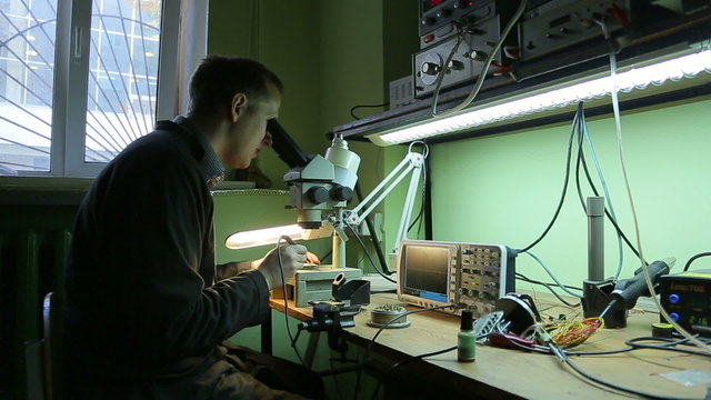 Scientist in the lab looking into a microscope and solder