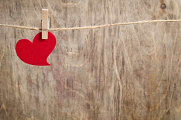 Red fabric heart hanging on the clothesline. On old wood backgro