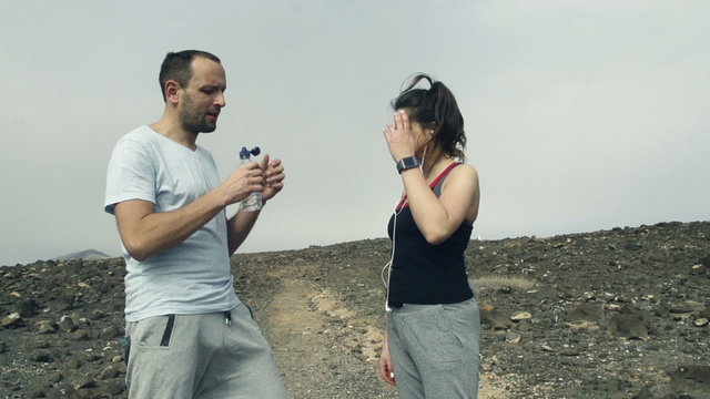 Joggers couple drinking water, resting and talking on desert