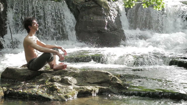 boy meditates sitting on a rock among  waterfalls - harmony - peace - into wild