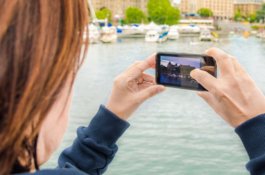 Woman Taking Photos with a Mobile Phone from a Ship in Harbour