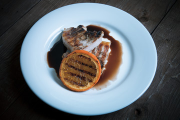 Grilled meat with orange on white ceramic plate on old wooden ta