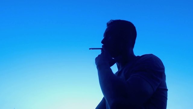 Young man smoking, relaxing at sunset