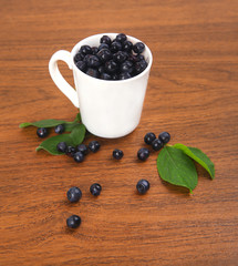 blueberries, currant with leaf in bowl, cup on wooden background