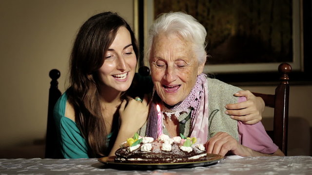 An young happy woman and his grandmother blow out her birthday candles