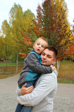 Папа с сыном на руках смотрят в даль в парке желтые листья