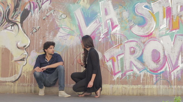 a young woman consoles a very sad man on the sidewalk - wall with grattiti