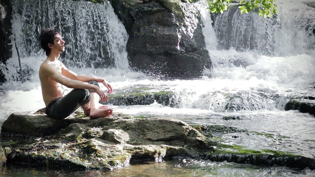 young man meditates sitting on a rock among small waterfalls - into the wild
