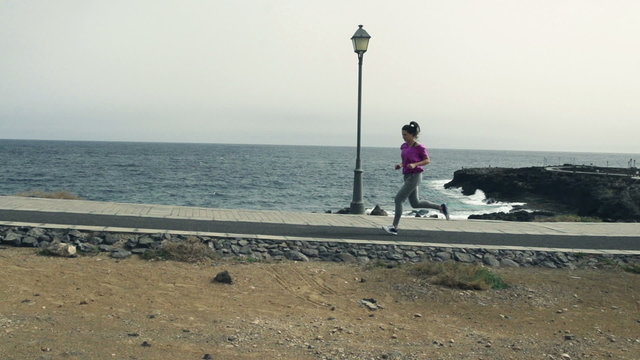 Young woman jogging through boardwalk by sea, slow motion