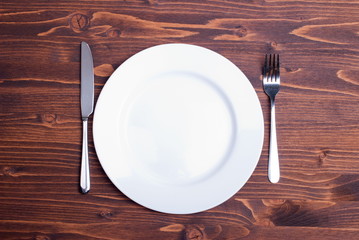 white plate and fork next to a knife on a wooden board top view