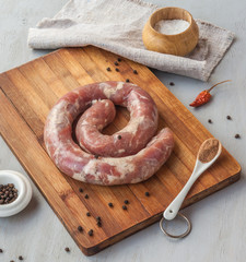 Ring of raw sausage on a cutting board with pepper