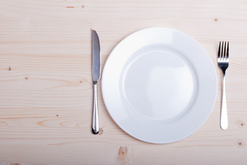 white plate and fork next to a knife on a wooden board top view