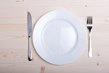 white plate and fork next to a knife on a wooden board top view