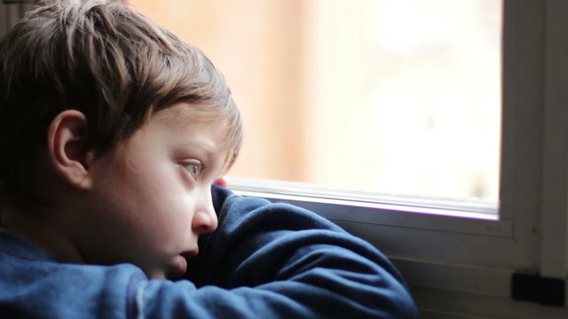 child sad and lonely looking through window