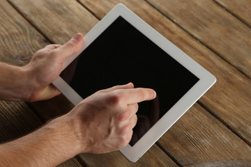 Hands holding tablet PC on wooden table background