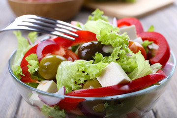 Greek salad in glass dish with fork on wooden table background
