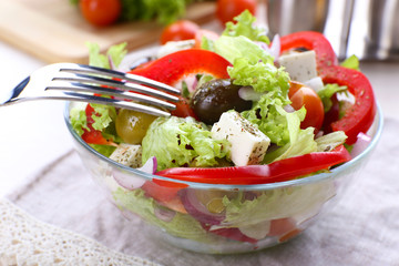 Greek salad in glass dish with fork and vegetables background