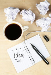Cup of coffee with crumpled paper and note Idea in notebook