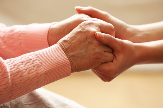 Old and young holding hands on light background