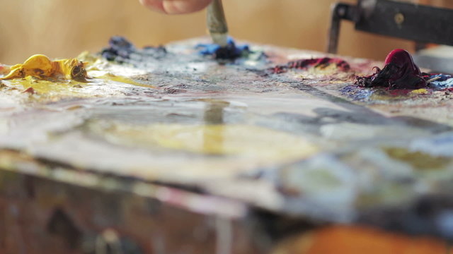 painter mixes with the brush colors in his palette