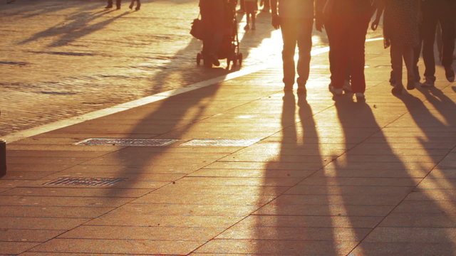 People walking at sunset, long shadows of people on the sidewalk in a city