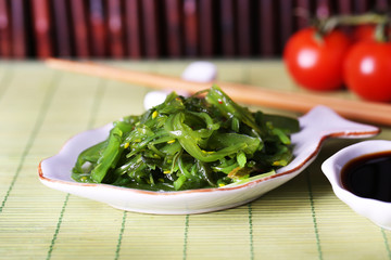 Seaweed salad in plate with bamboo on background