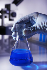 Laboratory glassware with blue liquid in hand of scientist