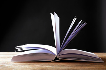 Open book on wooden surface and dark background