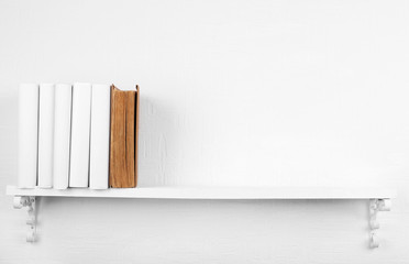 Blank books with brown one on bookshelf on white wall
