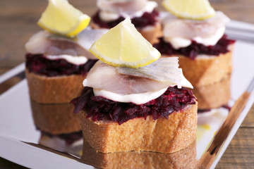 Rye toasts with herring and beets on tray on wooden background
