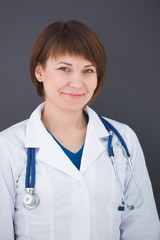 Portrait of happy young doctor on gray background looking at cam