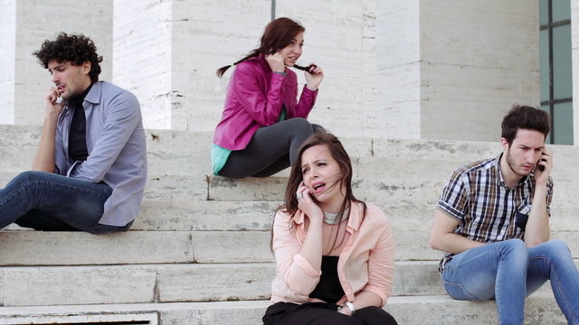 Four young people are on the phone sitting on a staircase - technology