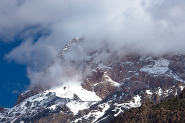 Clouds lie on the snow-covered tops of the rocks. Landscape