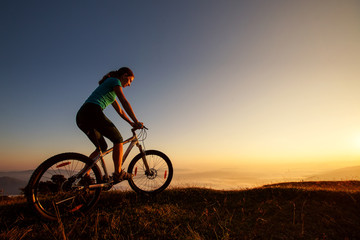 Fototapeta na wymiar Biker-girl at the sunset on mountains